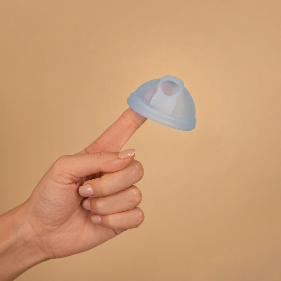 Hand holding a blue Mooneva Menstrual Disc on a beige background